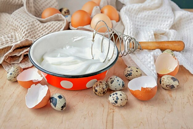 The beater eggs and a bowl with beaten egg whites on a wooden table