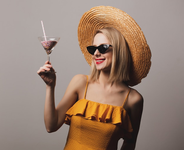 Beatiful girl with cocktail in hat and yellow dress