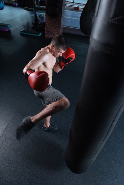 Sacca per battere. uomo dai capelli scuri con la tuta senza camicia e pantaloncini grigi che batte il sacco da boxe