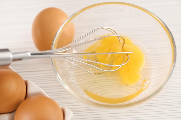 Beating up chicken eggs with whisk in glass bowl on table