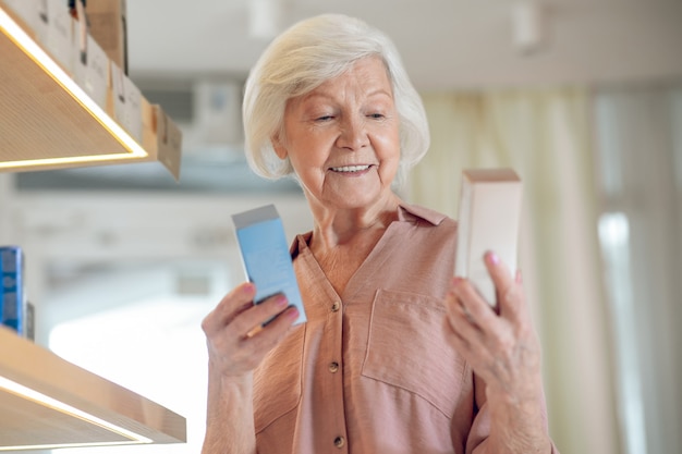 Beaty products. Gray-haired woman choosing beauty products and looking interested