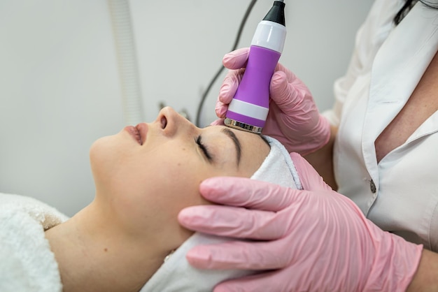 Косметолог проводит процедуру очистки аппаратным инструментом на женском лице в спа-салоне