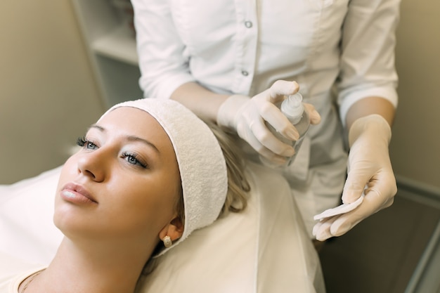 the beautician applies a cleanser to a cotton swab