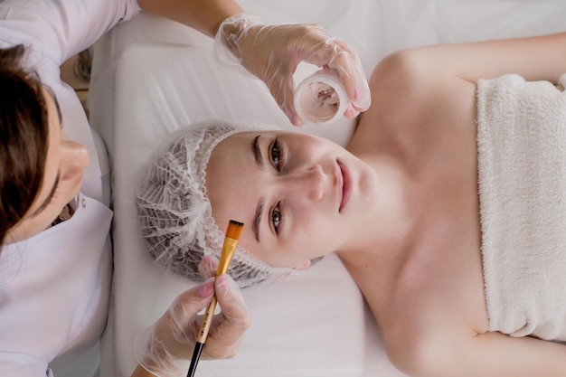 A beautician applies a mask to the skin of a woman's face for therapeutic purposes Rejuvenation acne treatment