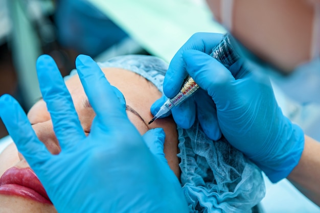 Beautician, applies a permanent makeup on the eyebrows. Eyebrow and lips tattoo