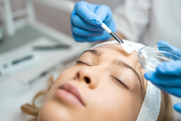 Beautician applying beauty oil mask on face skin using brush in spa salon