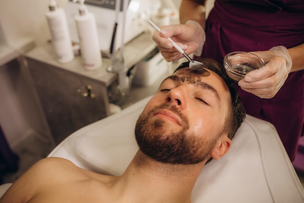 Photo beautician applying cosmetic mask on man's face in spa salon high quality photo