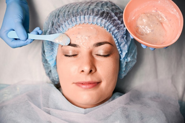 Beautician applying cosmetic mask on woman face