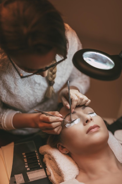 Beautician applying extended eyelashes to model at the beauty salon.