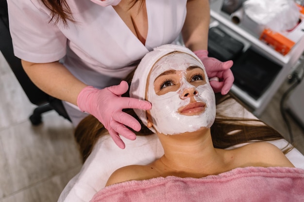 Beautician applying facial mask to the young lady view from the top