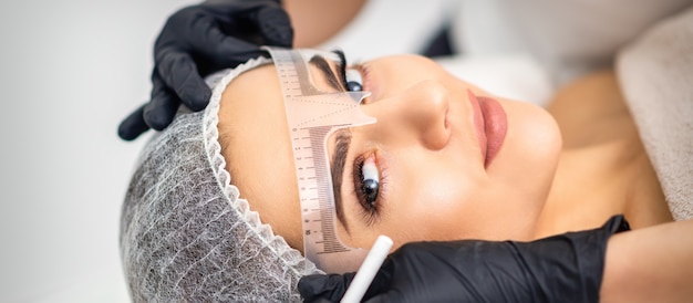 Beautician applying permanent makeup on eyebrows by tattoo machine tool