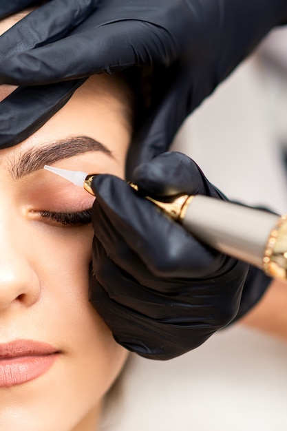 Beautician applying permanent makeup on eyebrows of young woman