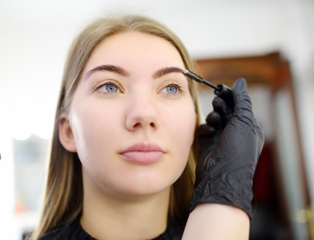 Foto l'estetista pettina le sopracciglia usando la spazzola speciale sul giovane bello modello del fronte. cura del viso e trucco