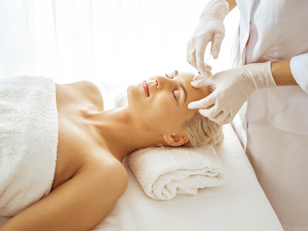 Beautician doctor hands doing beauty procedure to female face with syringe. Cosmetic medicine and surgery, beauty injections concept.