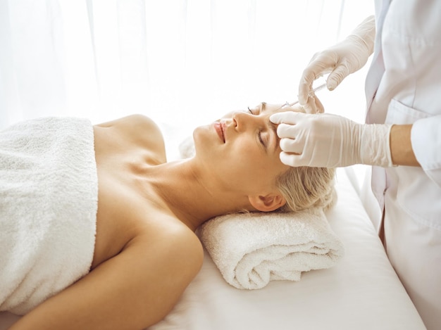 美容師は女性の顔に注射器を使って美容手術をします 美容医学と外科美容注射のコンセプト