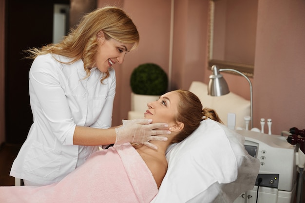 美容師の医者は美容クリニックで非外科的若返り手順の前に若い女性の顔を検査します