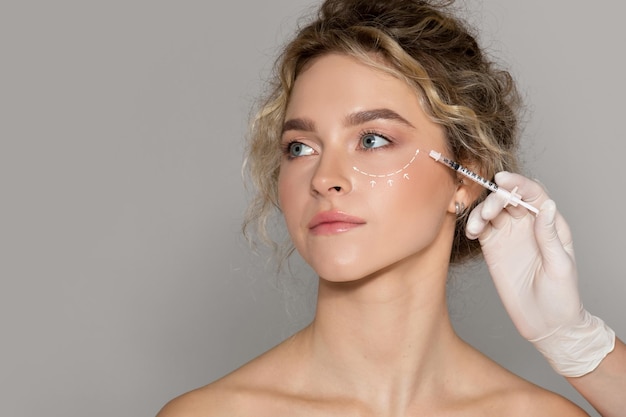 Фото Врач-косметолог делает инъекцию женщине с нарисованной линией под глазами даме, получающей мезотерапию