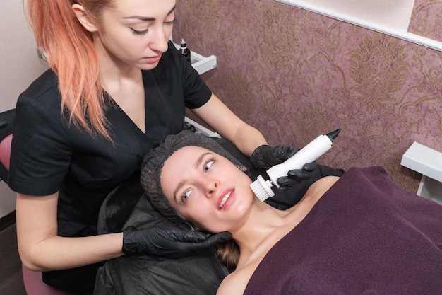 Врач-косметолог очищает лицо красивой пациентки вращающейся щеткой