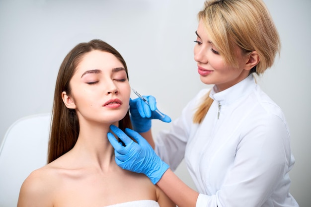 Beautician doctor with botulinum toxin syringe making injection to to remove crows feet Cheek volume enhance mesotherapy Antiaging treatment and face lift in cosmetology clinic