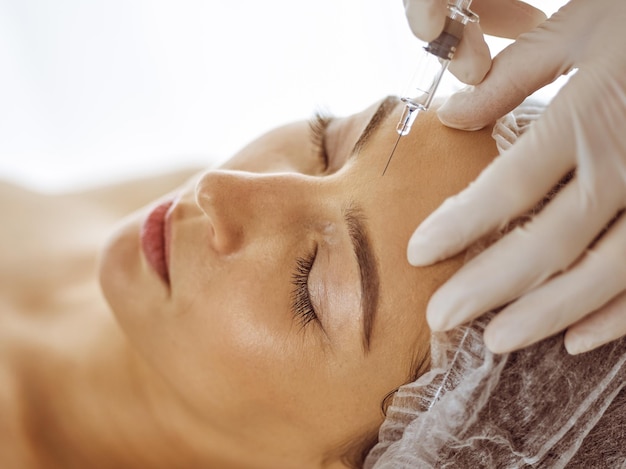 Photo beautician doing beauty procedure with syringe to face of young brunette woman. cosmetic medicine and surgery, beauty injections.