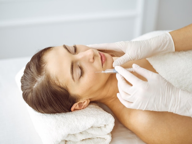 Beautician doing beauty procedure with syringe to face of young brunette woman. Cosmetic medicine and surgery, beauty injections.