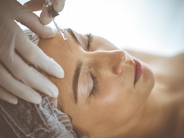 Beautician doing beauty procedure with syringe to face of young brunette woman. Cosmetic medicine and surgery, beauty injections.