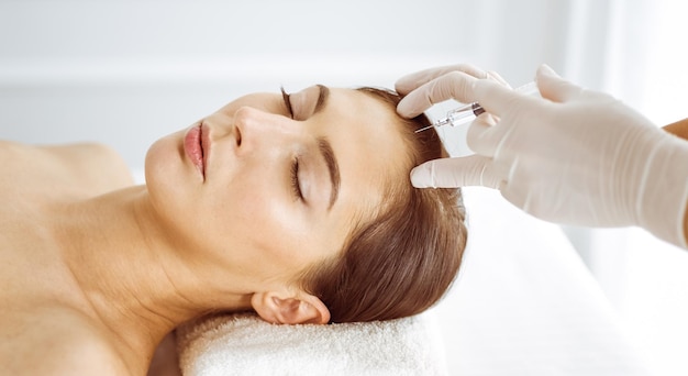 Косметолог делает косметическую процедуру со шприцем на лице молодой брюнетки. Косметическая медицина и хирургия, инъекции красоты.