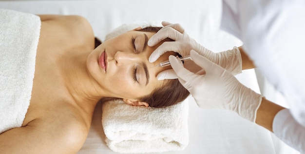 Beautician doing beauty procedure with syringe to face of young brunette woman. Cosmetic medicine and surgery, beauty injections.