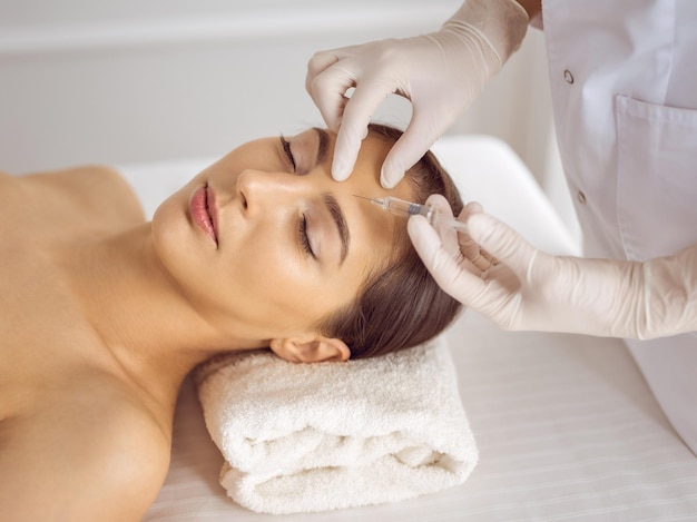 Beautician doing beauty procedure with syringe to face of young brunette woman. Cosmetic medicine and surgery, beauty injections.