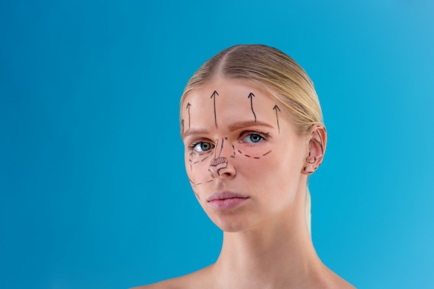 L'estetista disegna le linee di correzione sul viso della donna. prima dell'operazione di chirurgia plastica. isolato su blu