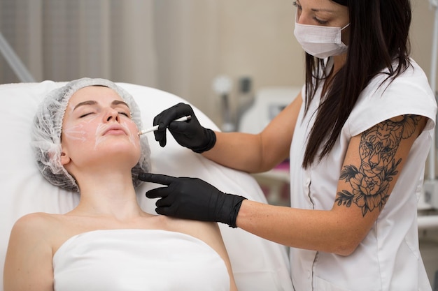 Beautician draws the contours of a white pencil on the face of the patient