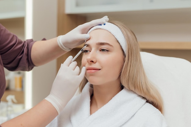 Beautician experts hands make injecting in female forehead