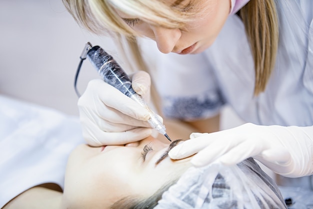 Beautician female applies permanent makeup on eyebrows tattoo eyebrows on beautiful models in a beauty parlor