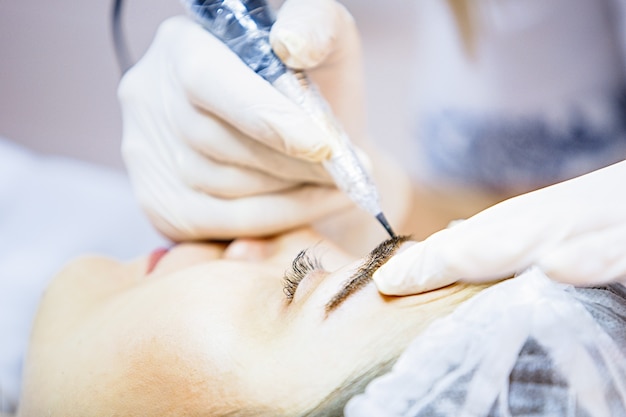 Beautician female applies permanent makeup on eyebrows tattoo eyebrows on beautiful models in a beauty parlor