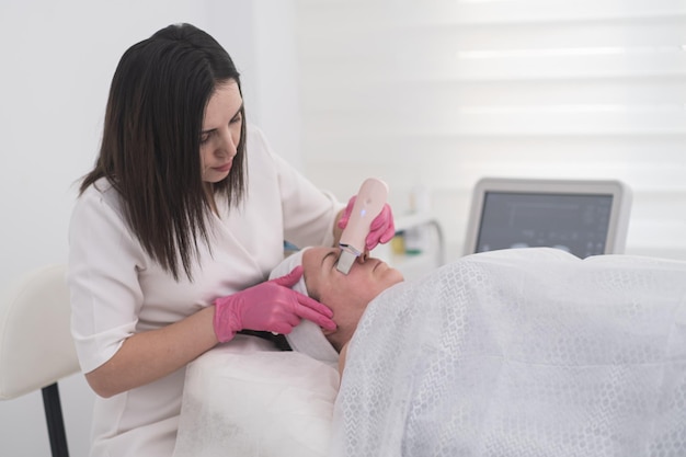 Beautician in gloves uses ultrasonic spatula for facial skin scrubbing and cleansing ultrasound