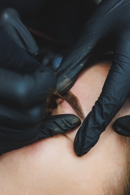 Beautician hand doing brow permanent makeup on an attractive female face