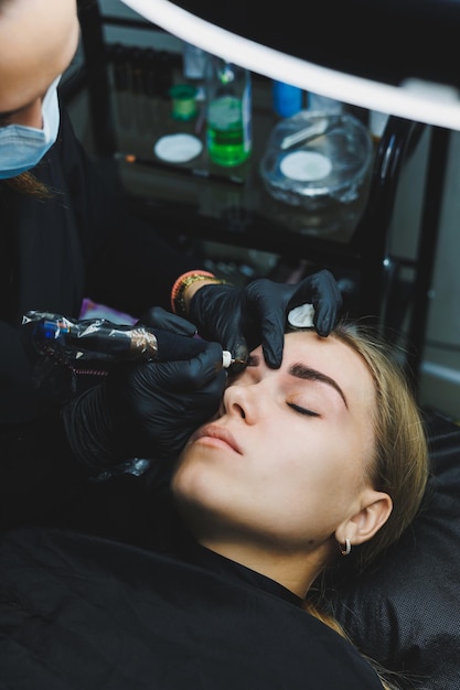 Рука косметолога делает перманентный макияж бровей на привлекательном женском лице