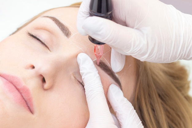 Beautician hands doing eyebrow tattoo