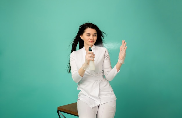 The beautician holds a bottle and sprays it into the air on turquoise