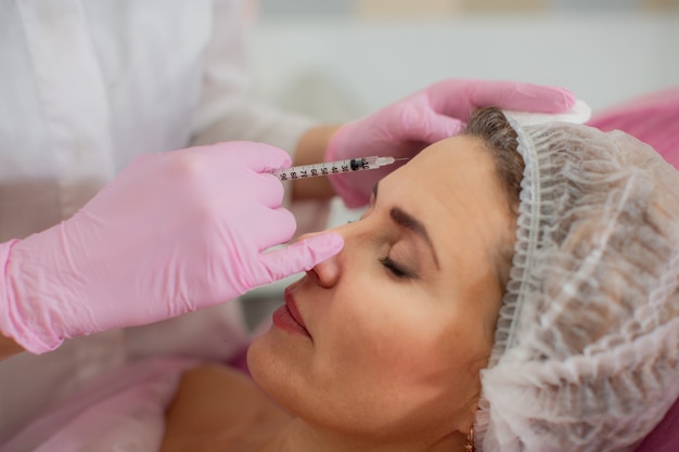 A beautician injects botox into the facial muscles of his patient's forehead.