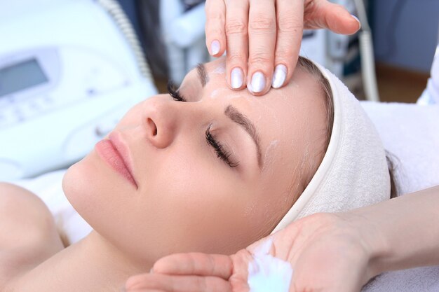 Beautician makes cleansing and exfoliating facial for beautiful girl. Beauty salon.