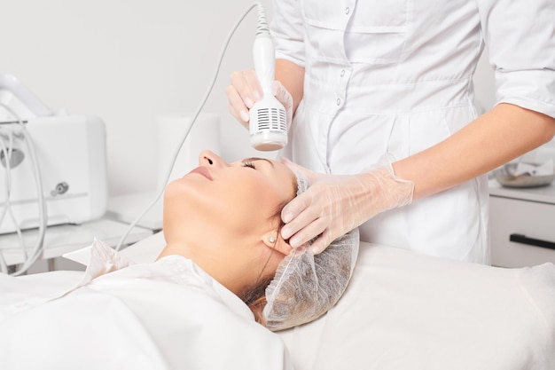 Beautician makes cryotherapy for rejuvenation woman face anti aging procedure in salon