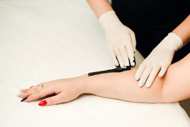 A beautician makes hair removal for clean, beautiful skin without hair. Depilation with black wax.