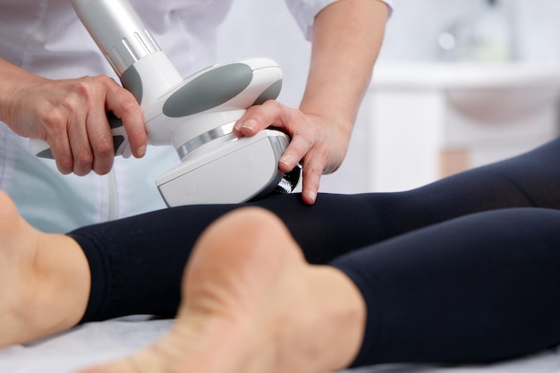 Photo beautician makes lpg calf massage of legs to young woman in black suit lymphatic drainage massage