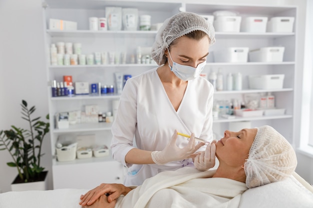 Beautician makes mesotherapy injections to a senior woman.
