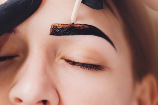 Beautician- makeup artist applies paint henna on previously plucked, design, trimmed eyebrows in a beauty salon in the session correction. Professional care for face.