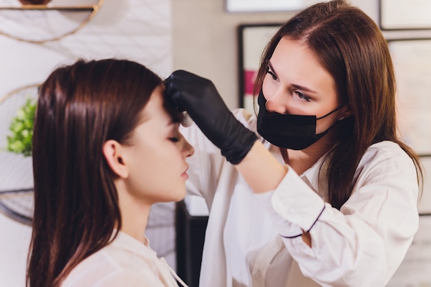 Beautician- makeup artist applies paint henna on previously plucked, design, trimmed eyebrows in a beauty salon in the session correction. Professional care for face.