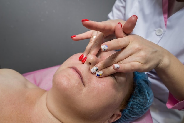 The beautician massages the face and head of an adult woman lying on a massage table. The concept of cosmetology, massage spa procedures.