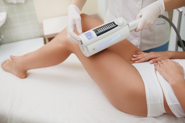 Beautician massaging legs of female client with endospheres apparatus at beauty salon