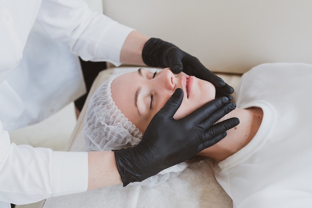 Beautician masseur doing facial massage to young woman